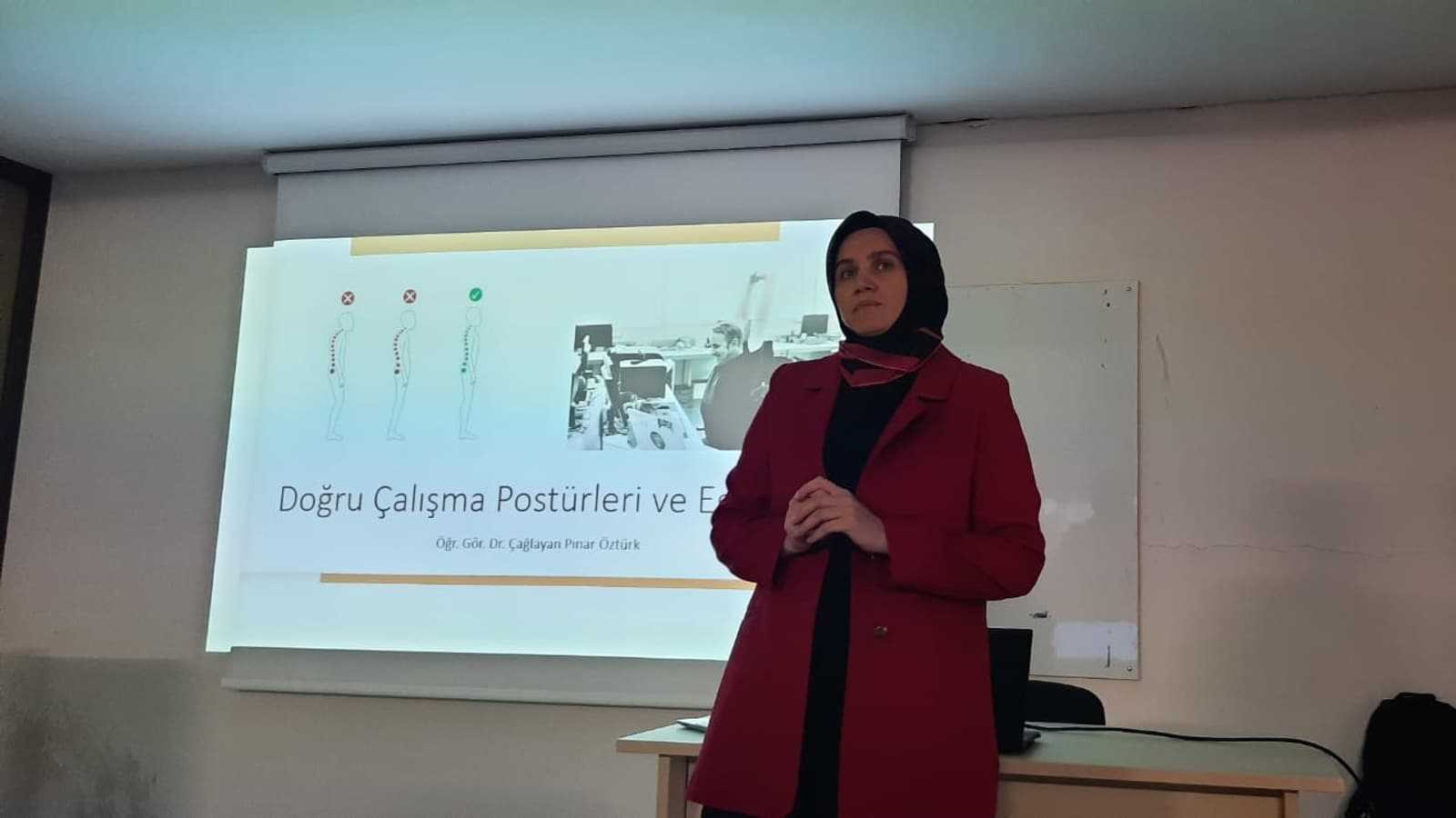 Fizyoterapist Dr. Çağlayan Pınar Öztürk, “Doğru Çalışma Postürleri ve Egzersiz” konferansında slaytın önünde duruyor. Süleyman Demirel Üniversitesi Adalet Meslek Yüksekokulu haberi, 16 Kasım 2023.